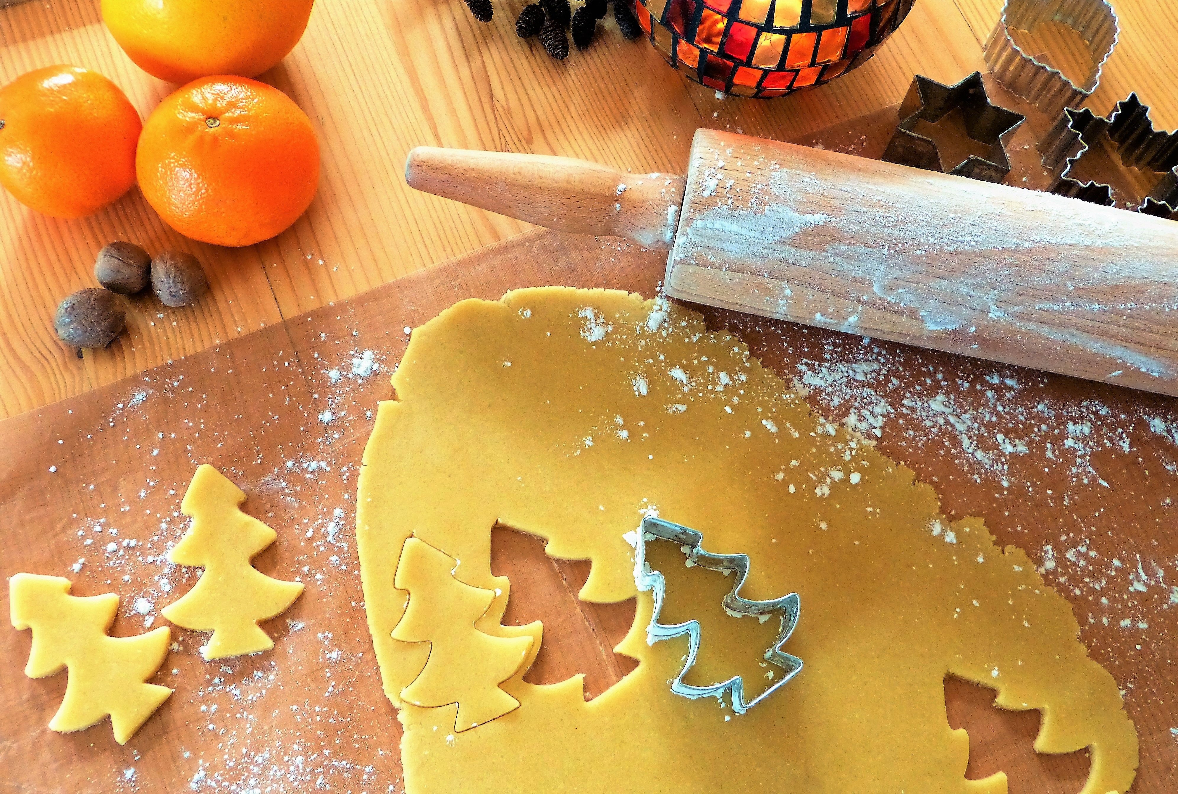An image of dough on a wooden counter with a rolling pin and a Christmas tree shaped cookie cutter